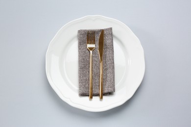 Photo of Plate, fork and knife on light grey table, top view