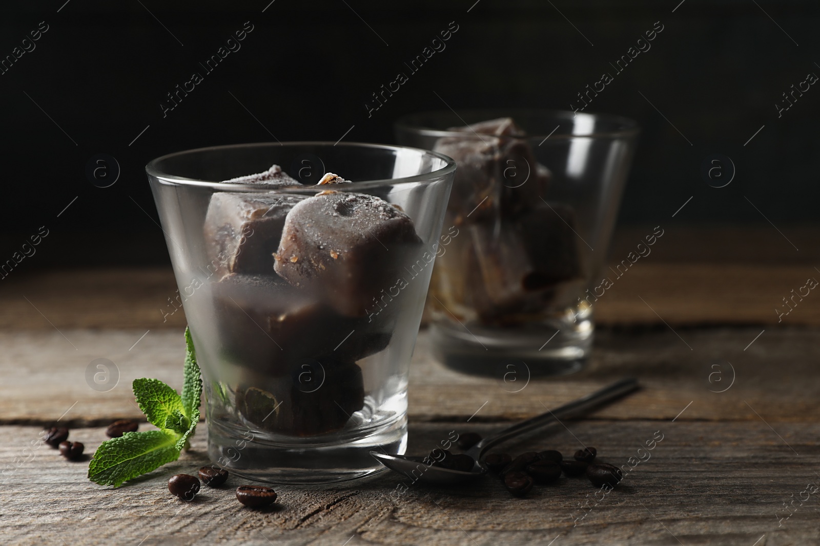 Photo of Glass of iced coffee cubes, beans and mint on wooden table, space for text