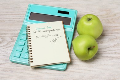 Notebook with calculated glycemic load for apples, calculator and fresh fruits on light wooden table