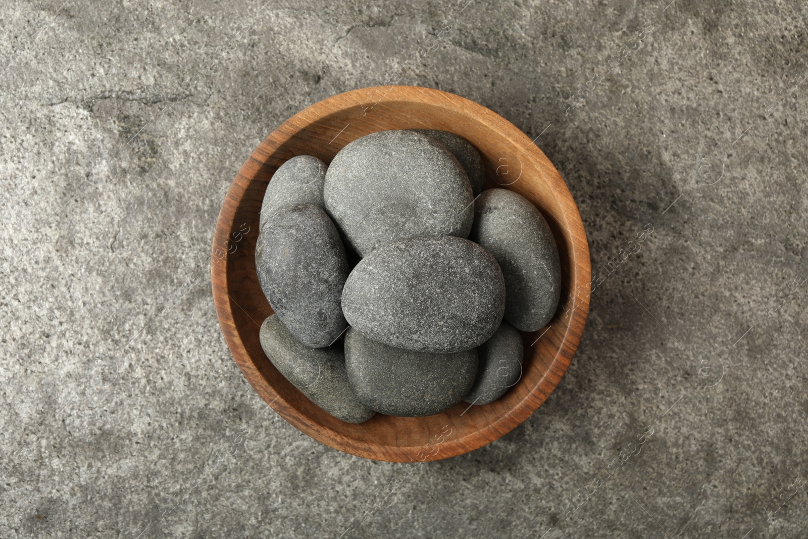 Photo of Bowl with spa stones on grey table, top view