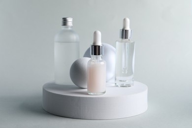 Stylish presentation of bottles with cosmetic serums on light grey background