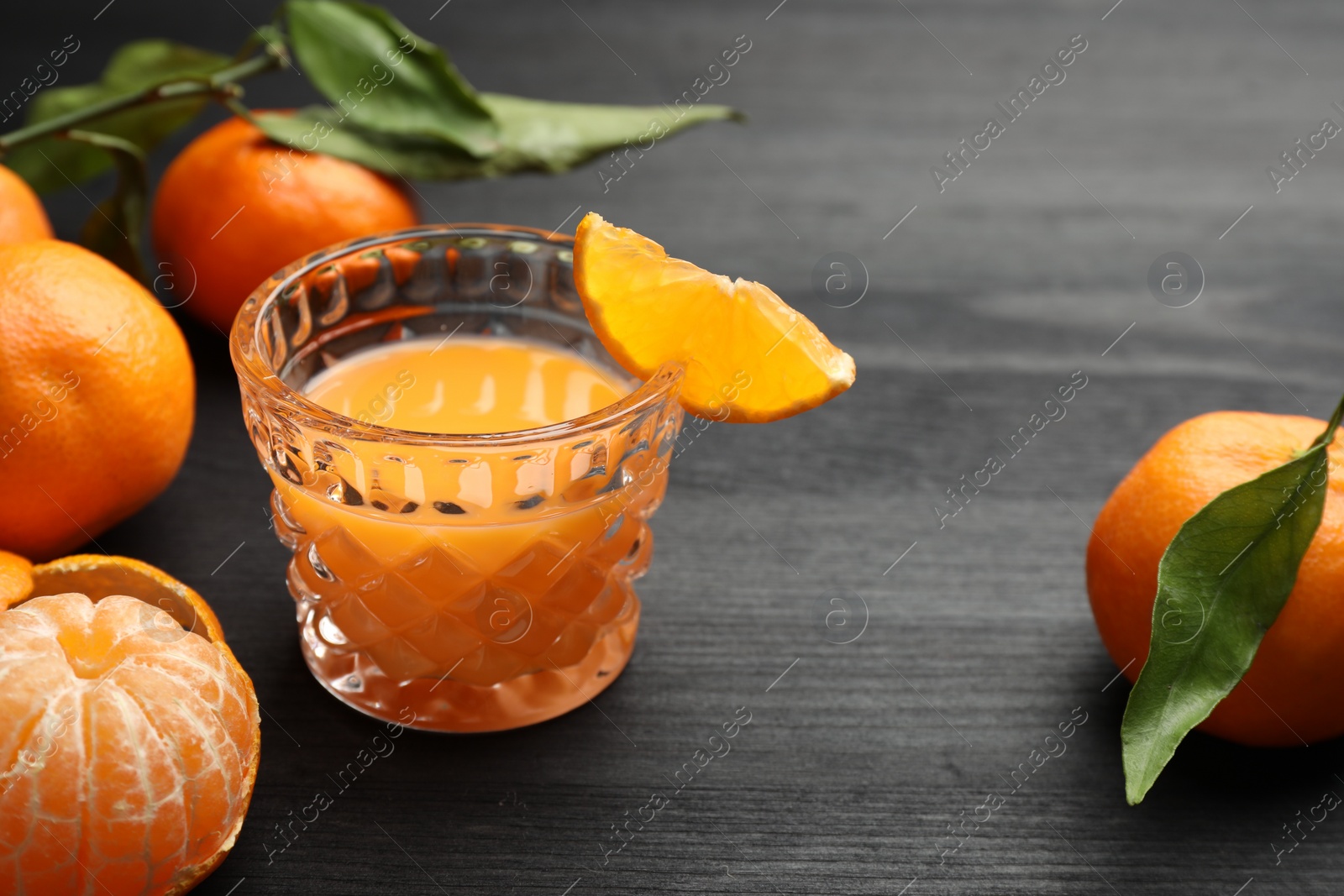 Photo of Tasty tangerine liqueur in glass and fresh fruits on black wooden table. Space for text