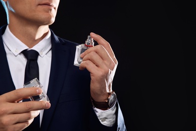 Photo of Young man with perfume bottle on black background, closeup. Space for text