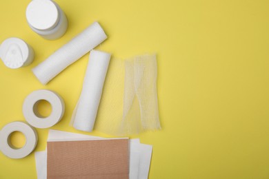 Photo of White bandage rolls and medical supplies on yellow background, flat lay. Space for text