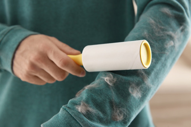 Man removing hair from green sweatshirt with lint roller on light background, closeup