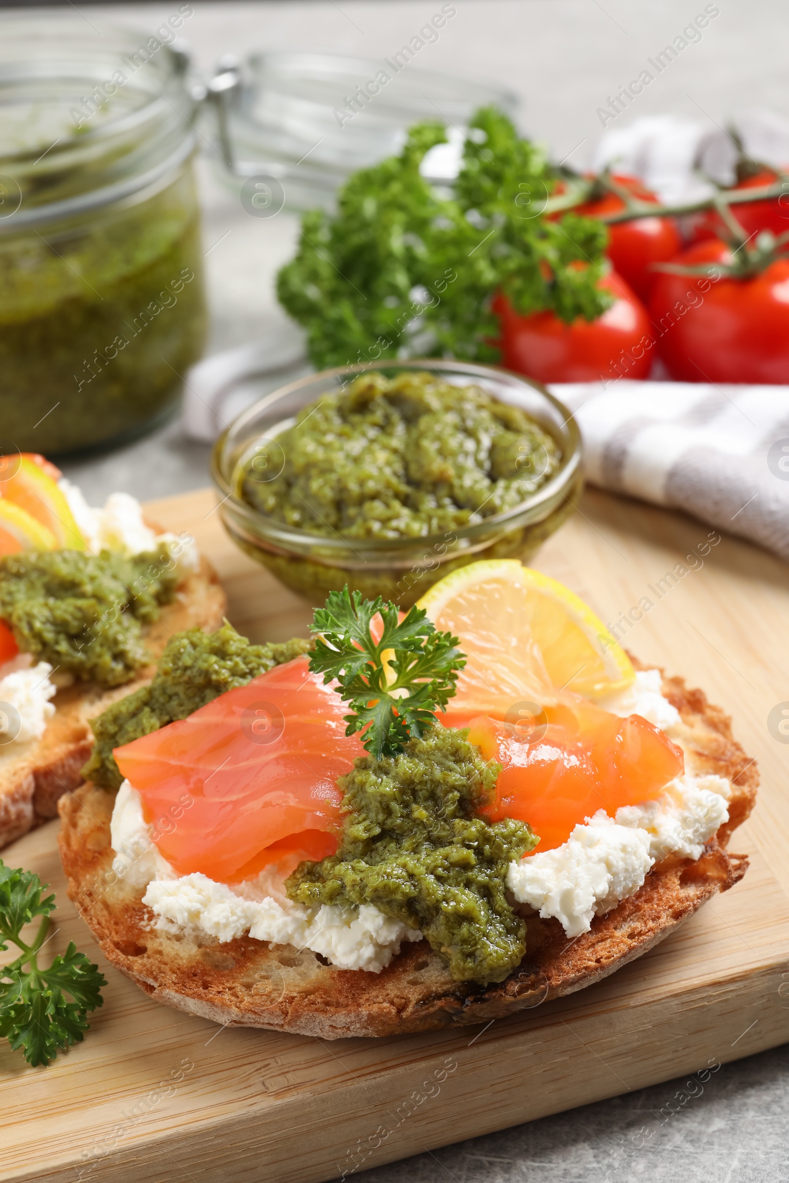 Photo of Delicious bruschetta with salmon, cream cheese and pesto sauce on table, closeup