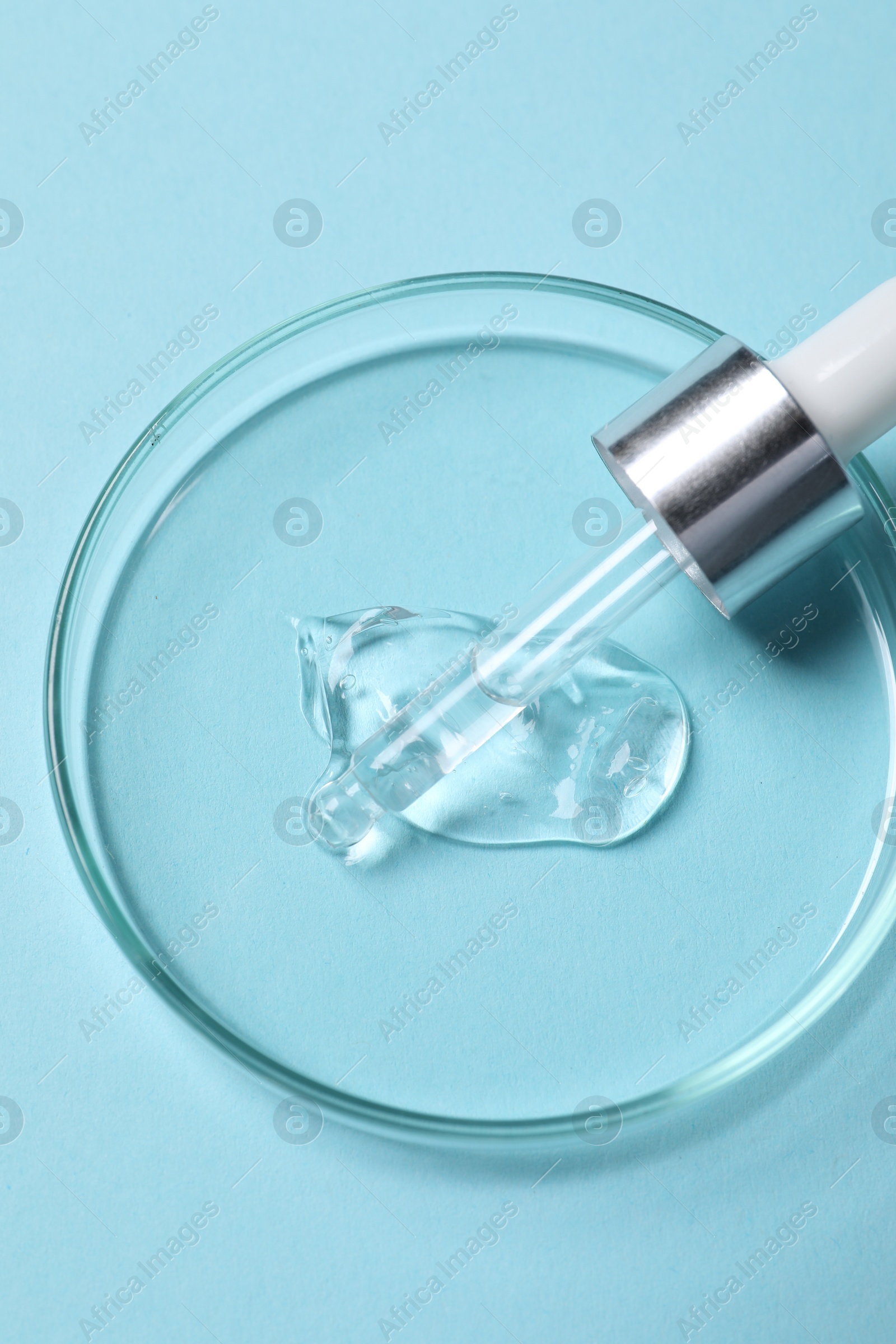 Photo of Petri dish with sample of cosmetic serum and pipette on light blue background, top view