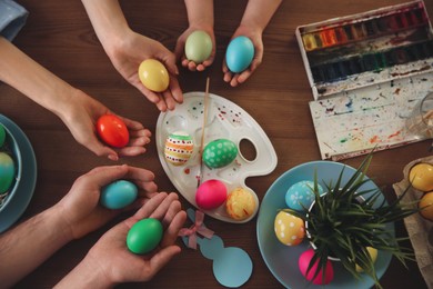 Photo of Father, mother and their child painting Easter eggs at wooden table, top view