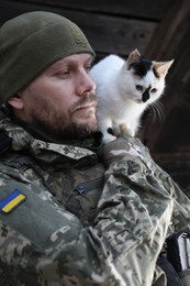 Ukrainian soldier rescuing animal. Little stray cat on man's shoulder, closeup