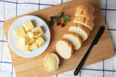 Photo of Cut baguette with fresh butter on checkered tablecloth, top view