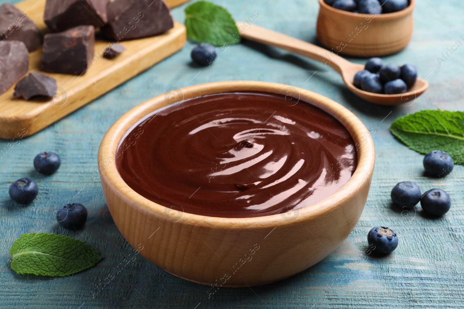 Photo of Delicious chocolate cream with blueberries and mint on light blue wooden table