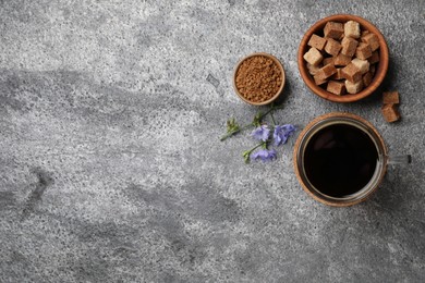 Glass cup of delicious chicory drink, granules, brown sugar and flowers on grey table, flat lay. Space for text