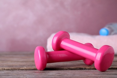 Stylish dumbbells and towel on table against color background, space for text. Home fitness