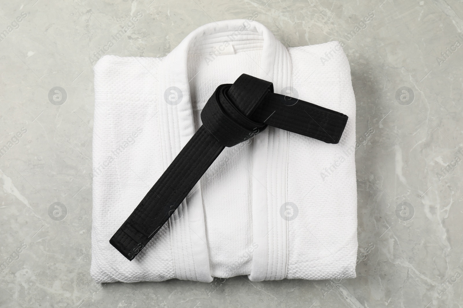 Photo of Black karate belt and white kimono on gray marble background, top view