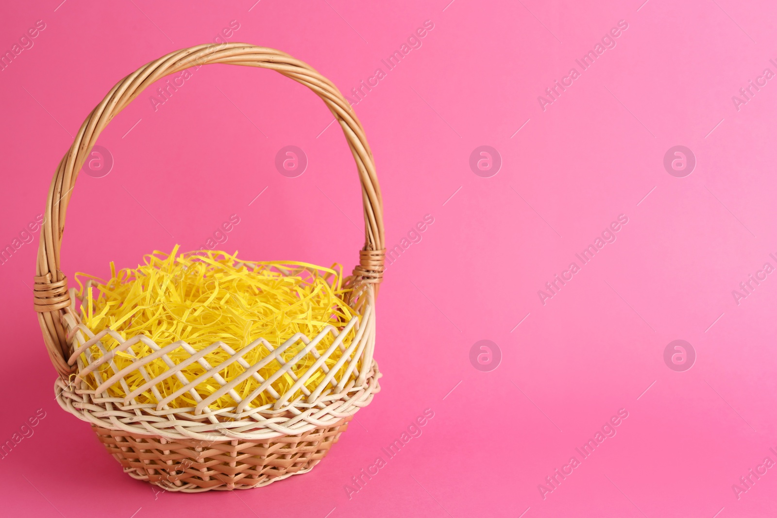 Photo of Easter basket with yellow paper filler on pink background, space for text