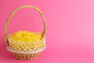 Easter basket with yellow paper filler on pink background, space for text