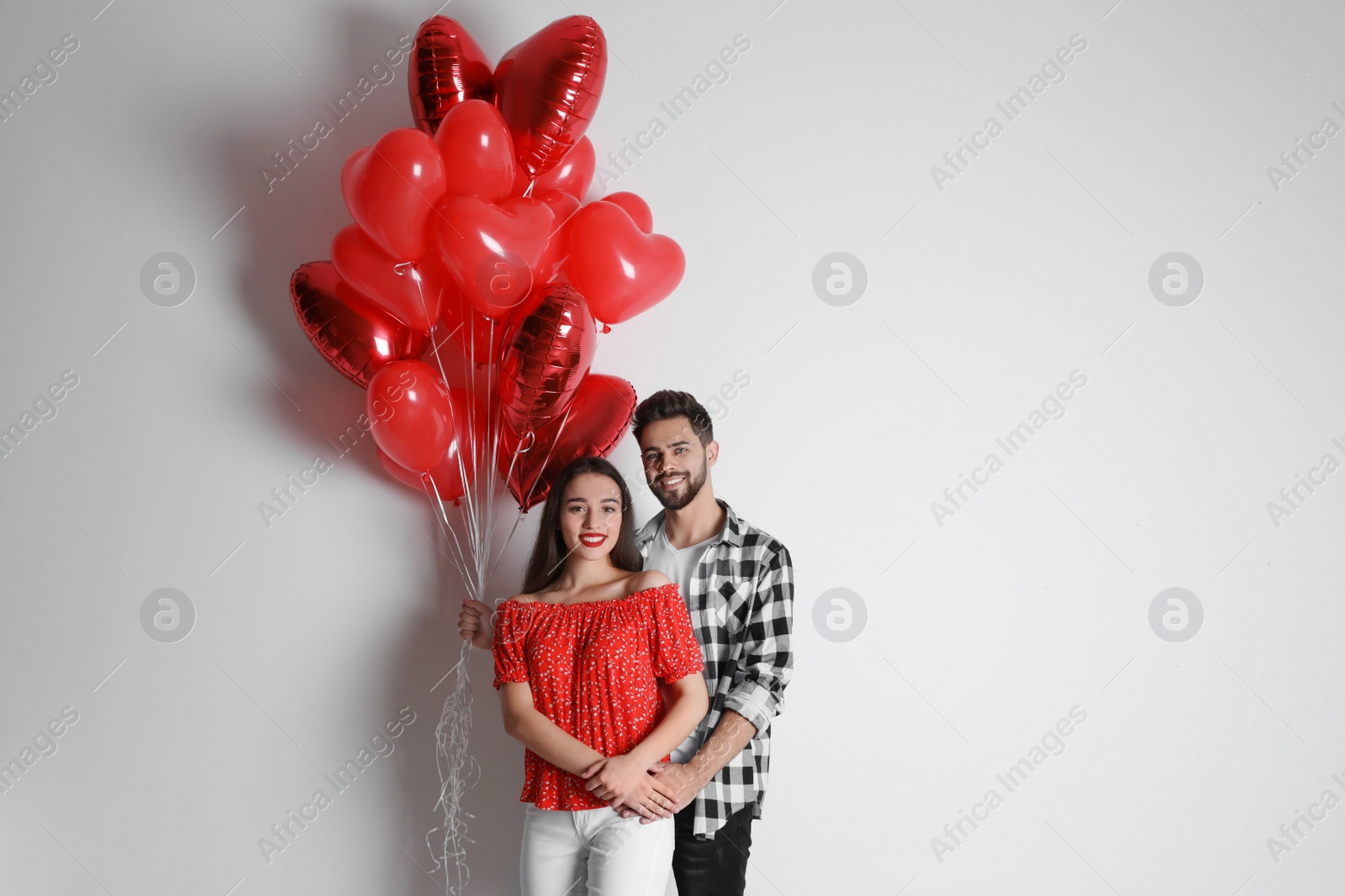 Photo of Happy young couple with heart shaped balloons on light background. Valentine's day celebration