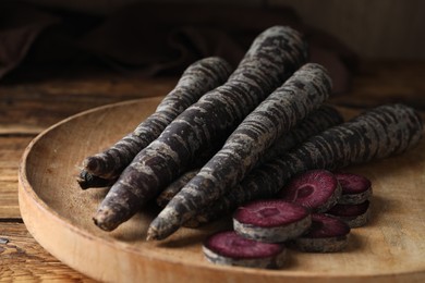 Raw black carrots on wooden plate, closeup