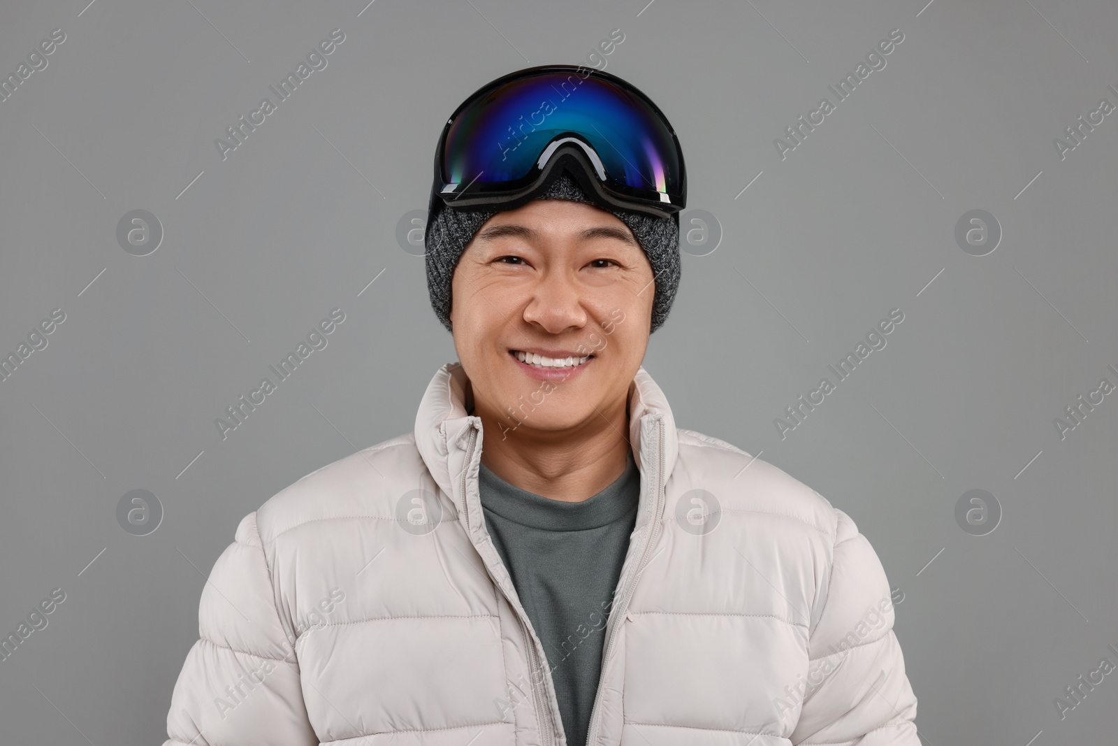 Photo of Winter sports. Happy man with ski goggles on grey background