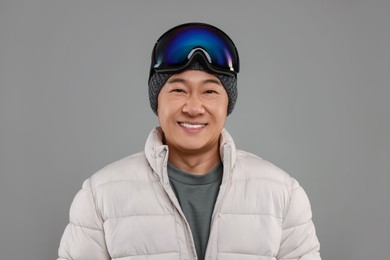 Photo of Winter sports. Happy man with ski goggles on grey background