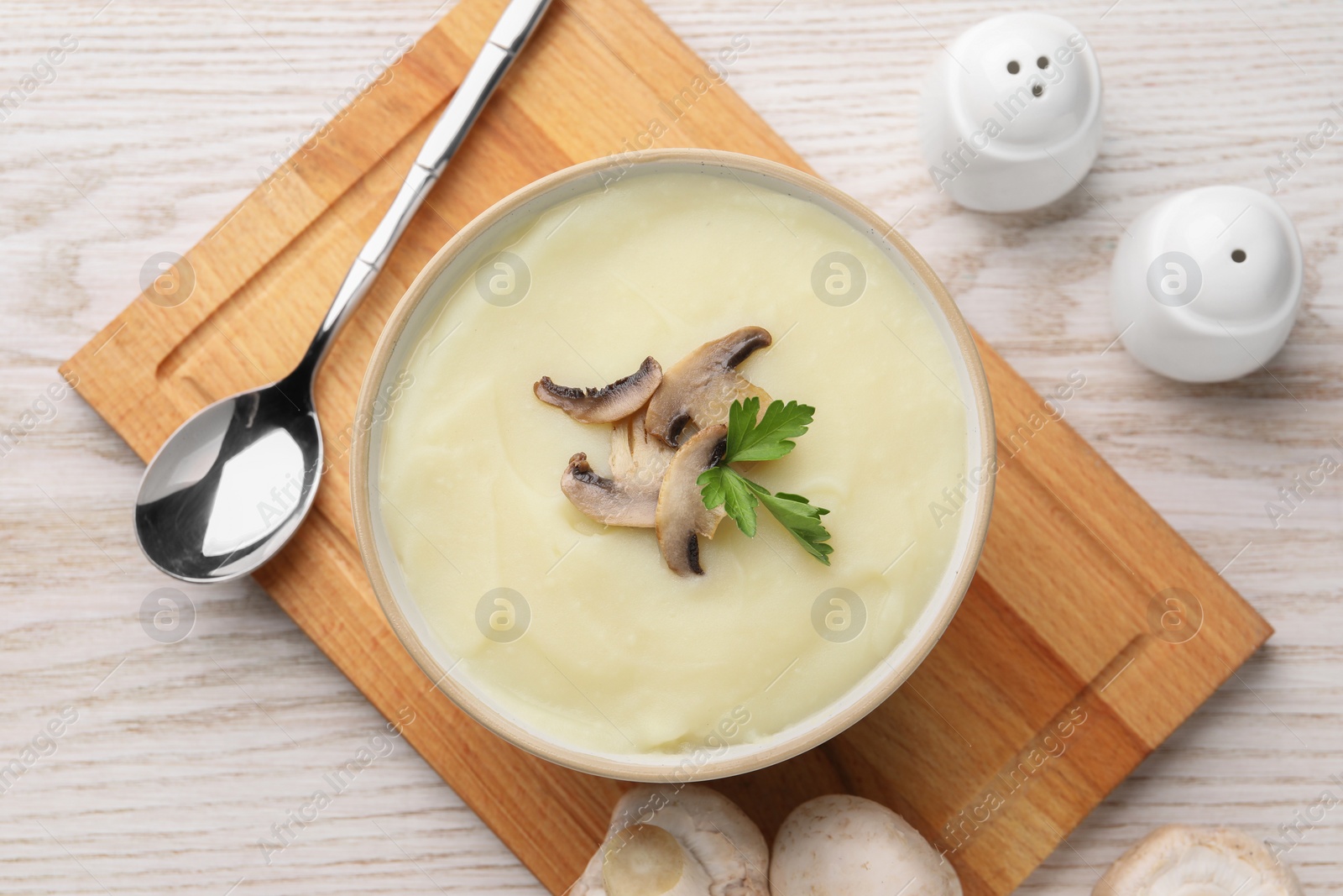 Photo of Bowl of tasty cream soup with mushrooms, parsley and spoon on light wooden table, flat lay