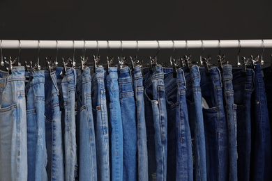 Photo of Rack with different jeans on dark grey background