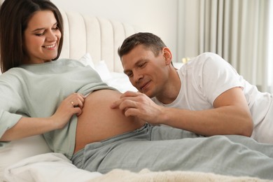 Photo of Young pregnant woman with her husband in bedroom