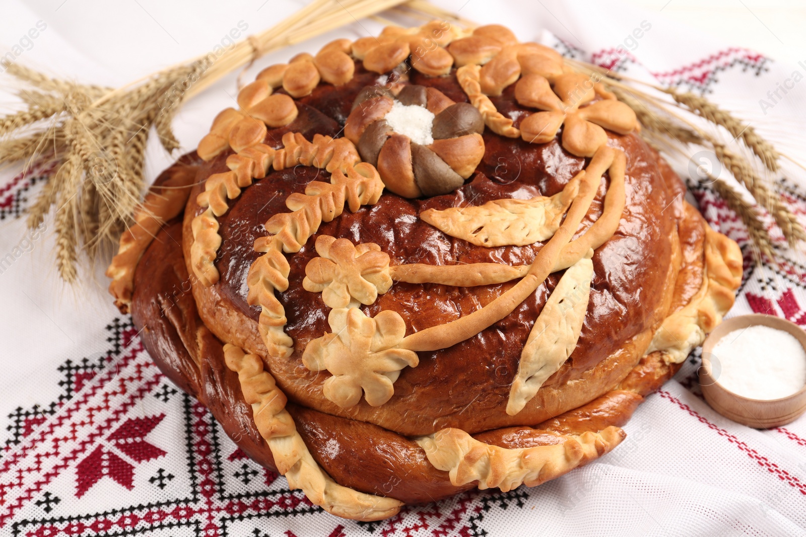Photo of Korovai with wheat spikes on rushnyk, closeup. Ukrainian bread and salt welcoming tradition