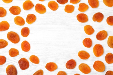 Photo of Frame made of dried apricots on white wooden table, top view with space for text. Healthy fruit