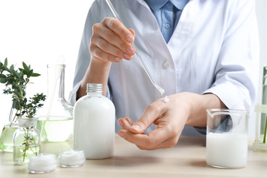 Photo of Woman applying natural cream onto hand in cosmetic laboratory, closeup