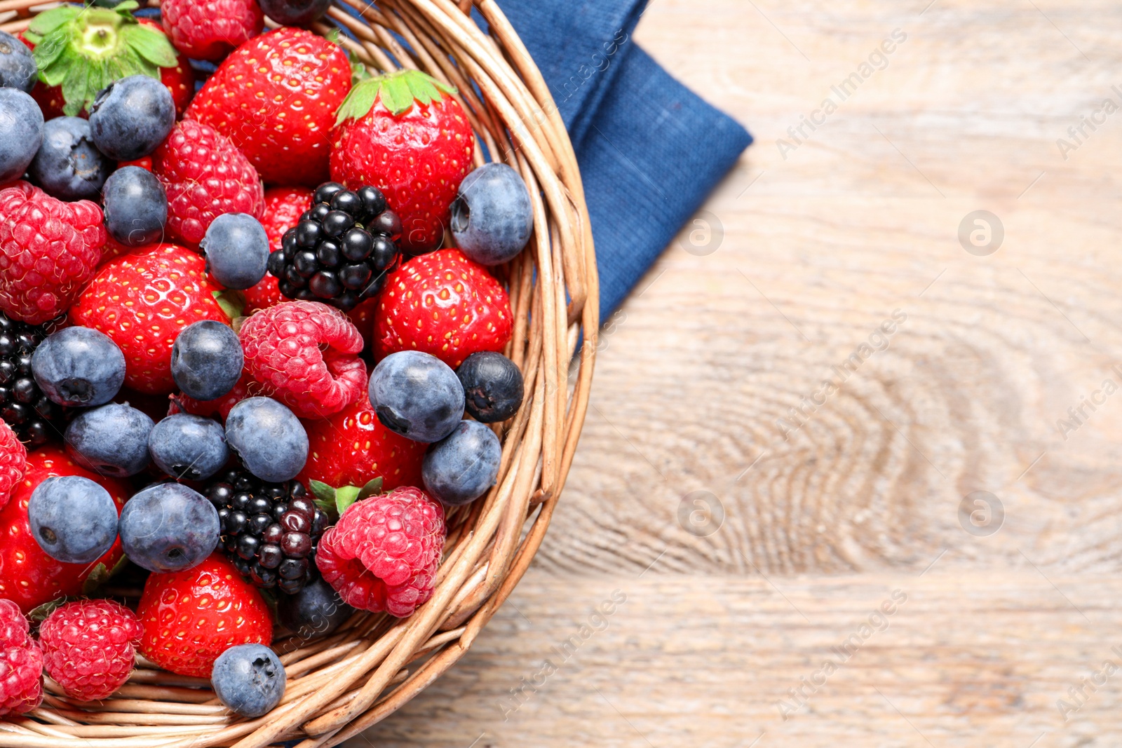 Photo of Many different fresh ripe berries in wicker basket on wooden table, top view. Space for text