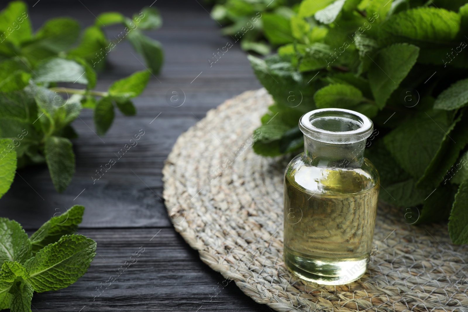 Photo of Bottle of mint essential oil and green leaves on black wooden table, closeup. Space for text