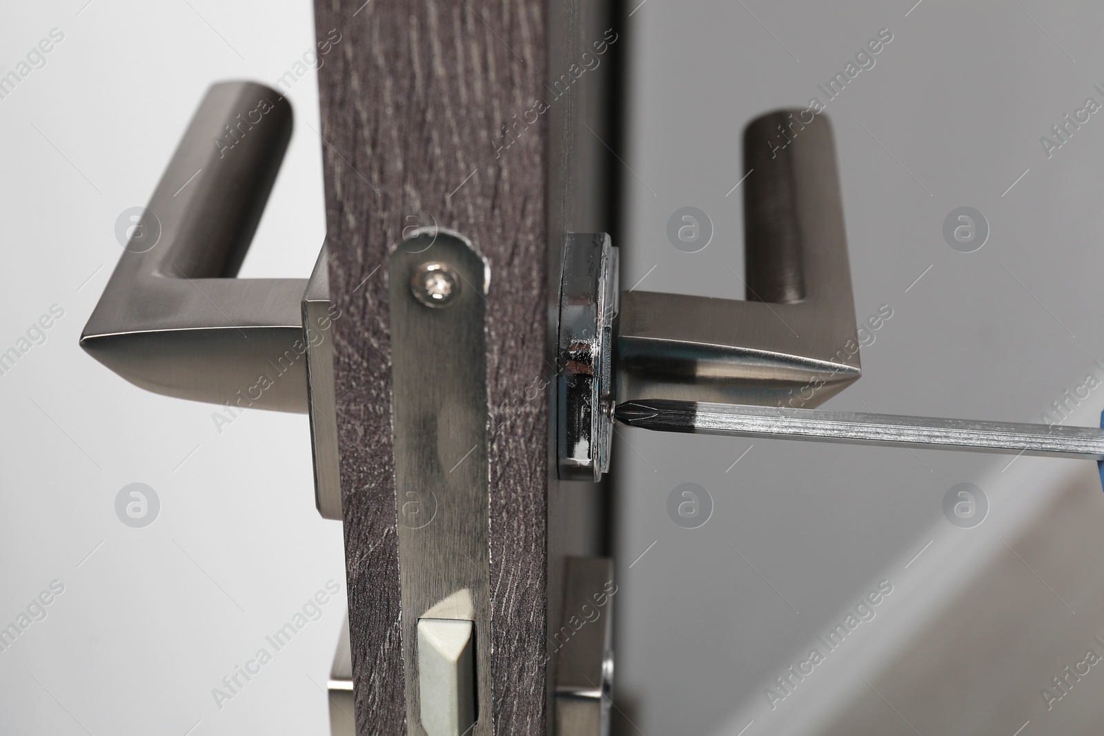 Photo of Repairing door handle with screwdriver indoors, closeup