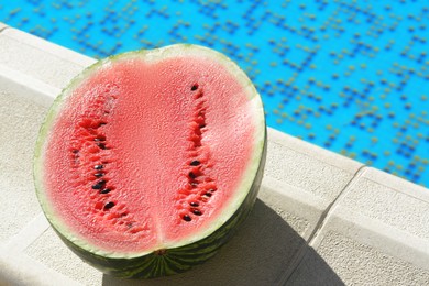 Photo of Half of fresh juicy watermelon near swimming pool outdoors. Space for text