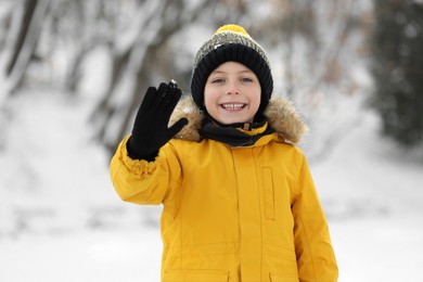 Cute little boy greeting someone in snowy park on winter day