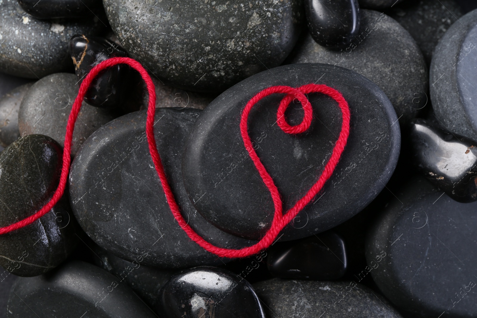 Photo of Heart made of thread on pebble stones, top view