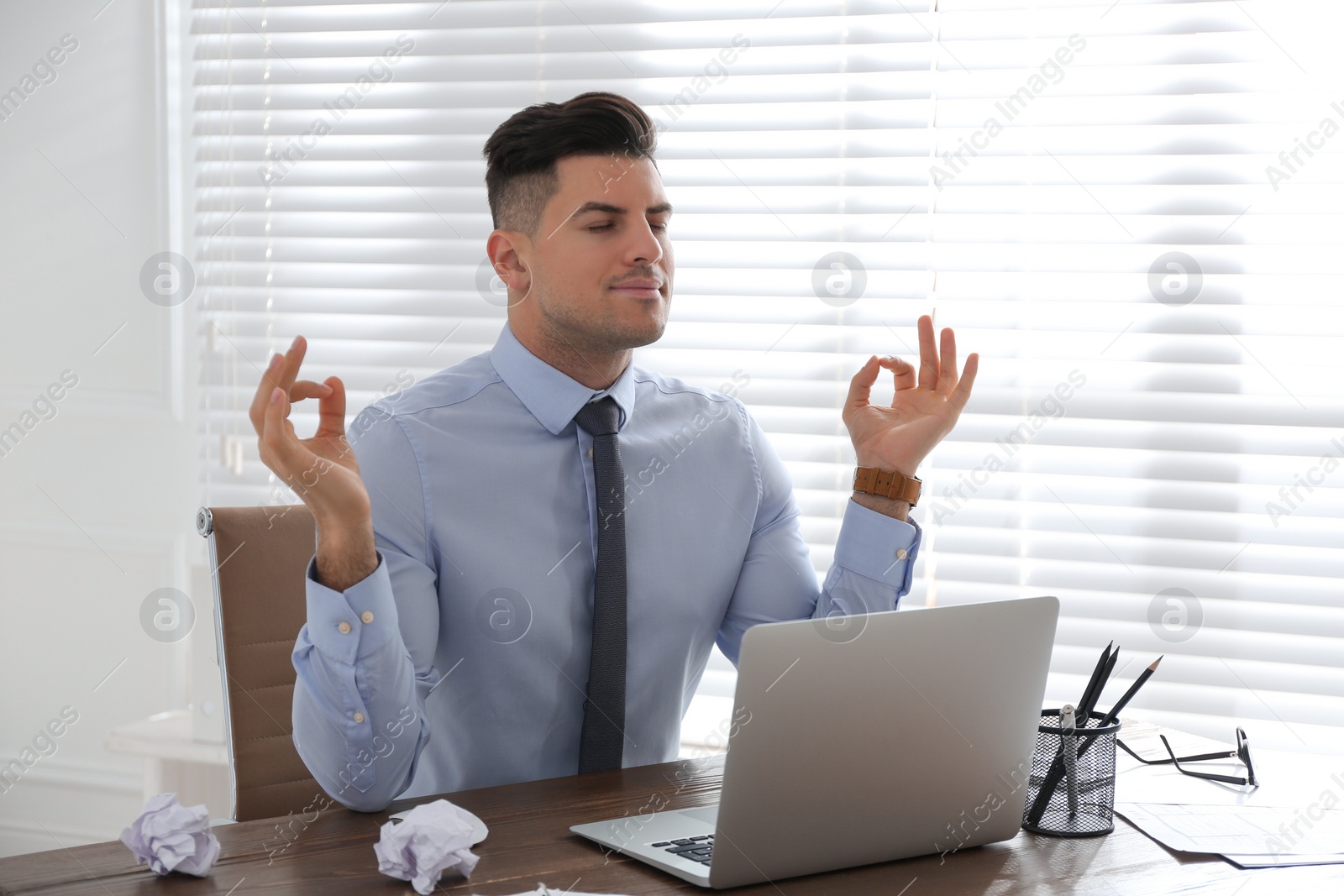 Photo of Businessman meditating at workplace in office. Stress relieving exercise