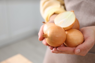 Photo of Woman holding golden onions indoors, closeup. Space for text