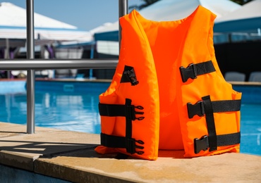 Photo of Bright orange life jacket near swimming pool