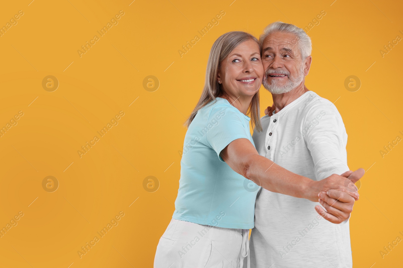 Photo of Senior couple dancing together on orange background, space for text