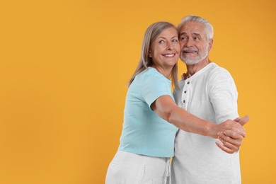 Photo of Senior couple dancing together on orange background, space for text