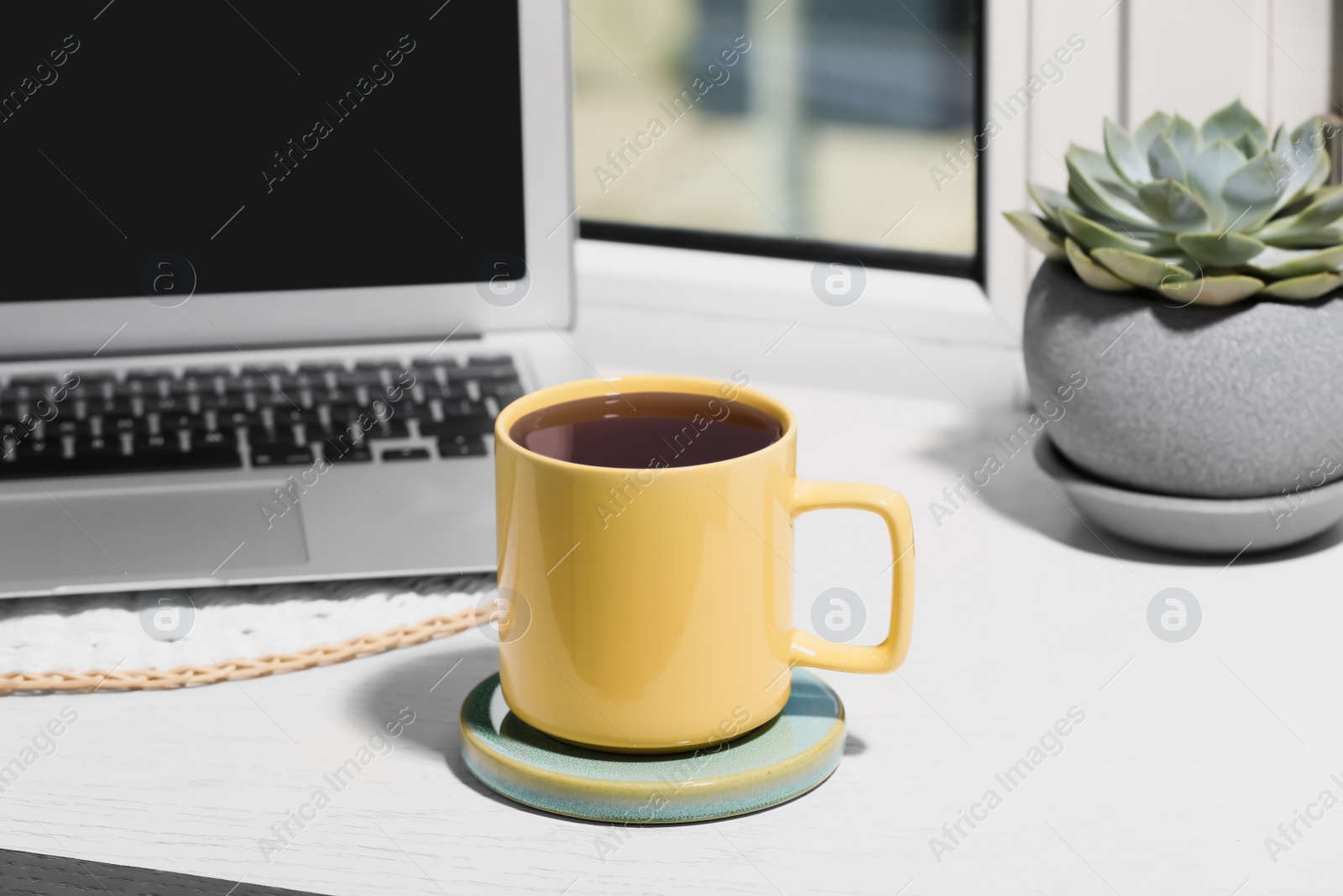 Photo of Cup of tea, laptop and succulent on wooden window sill