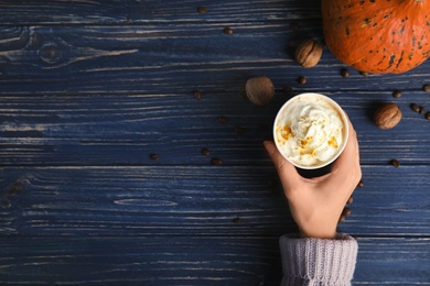 Photo of Woman holding paper cup with pumpkin spice latte on wooden background, top view. Space for text