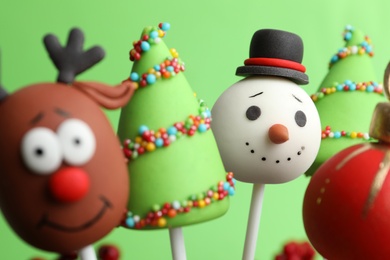 Delicious Christmas themed cake pops on green background, closeup