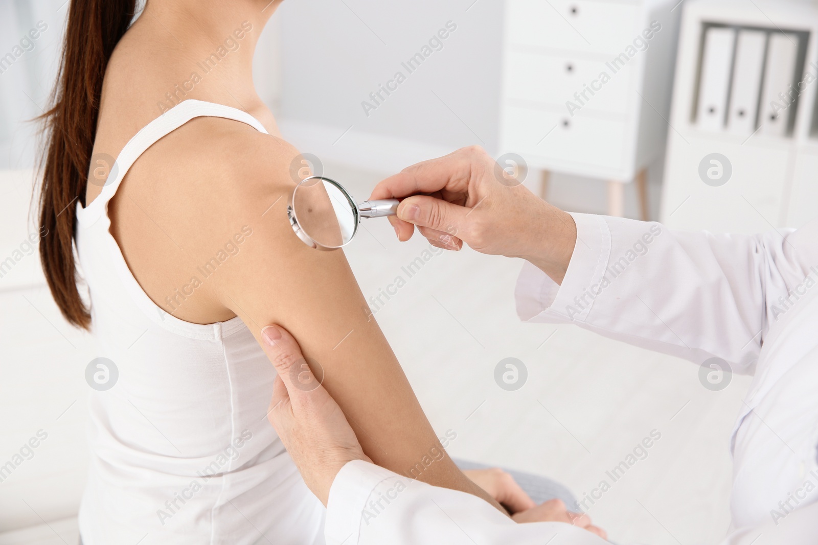 Photo of Dermatologist examining patient's birthmark with magnifying glass in clinic, closeup