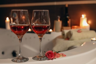 Photo of Wine in glasses and rose on edge of bath indoors. Romantic atmosphere