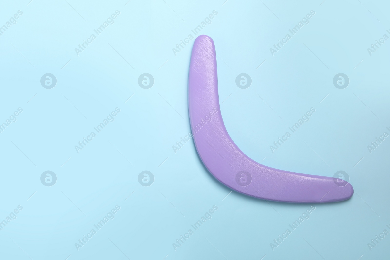 Photo of Lilac wooden boomerang on light blue background, top view. Space for text