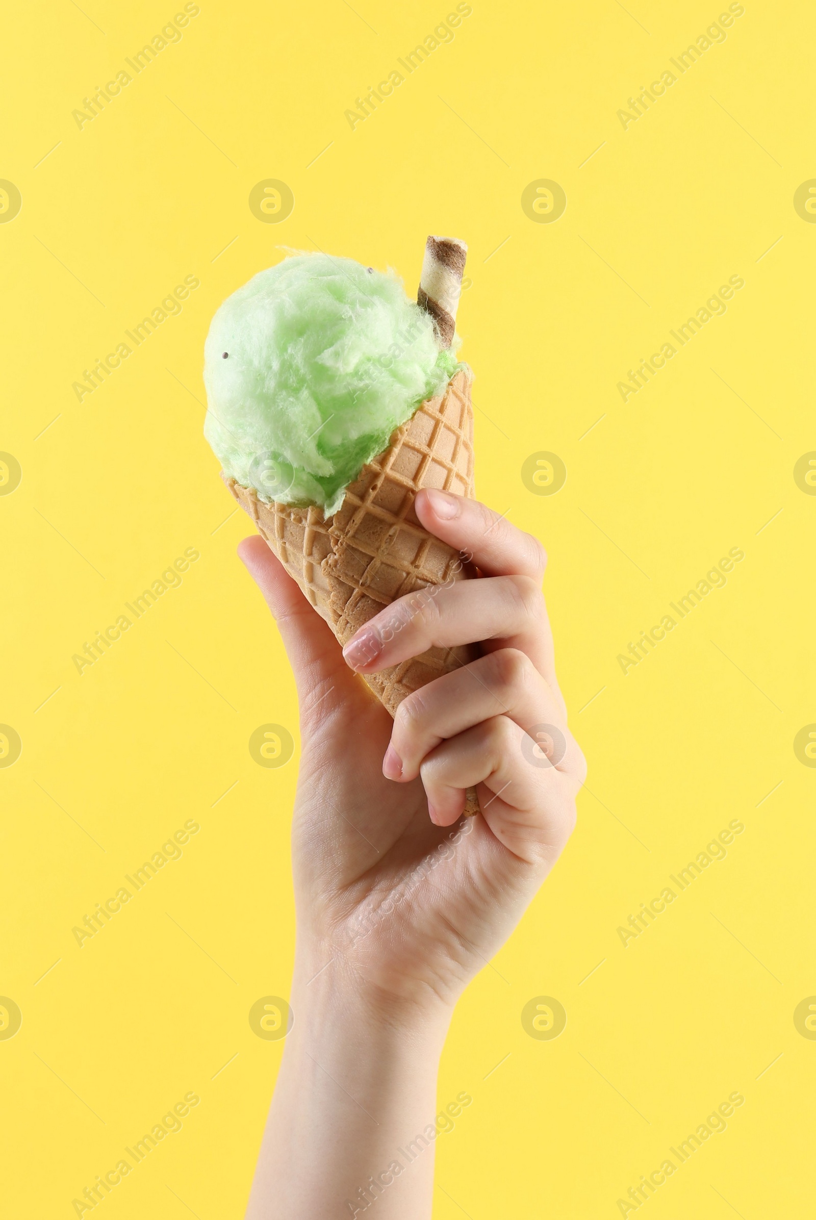 Photo of Woman holding waffle cone with cotton candy on yellow background, closeup