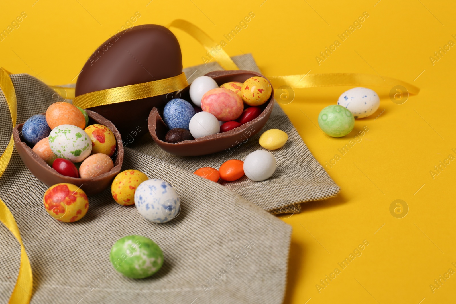 Photo of Whole and halves of chocolate eggs with colorful candies on yellow background