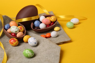 Photo of Whole and halves of chocolate eggs with colorful candies on yellow background